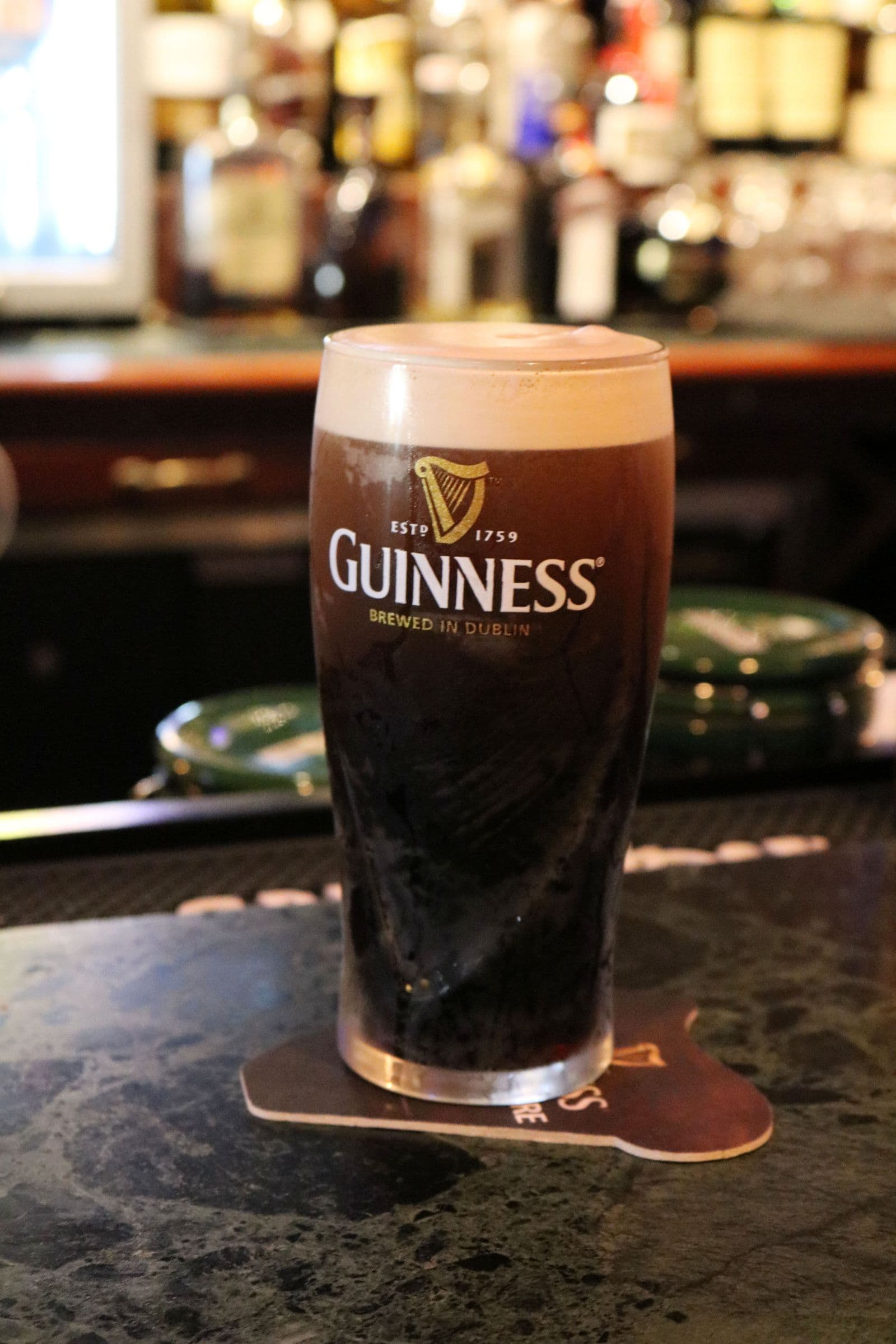 Una pinta de cerveza Guinness sobre la barra de un pub con botellas de licor al fondo