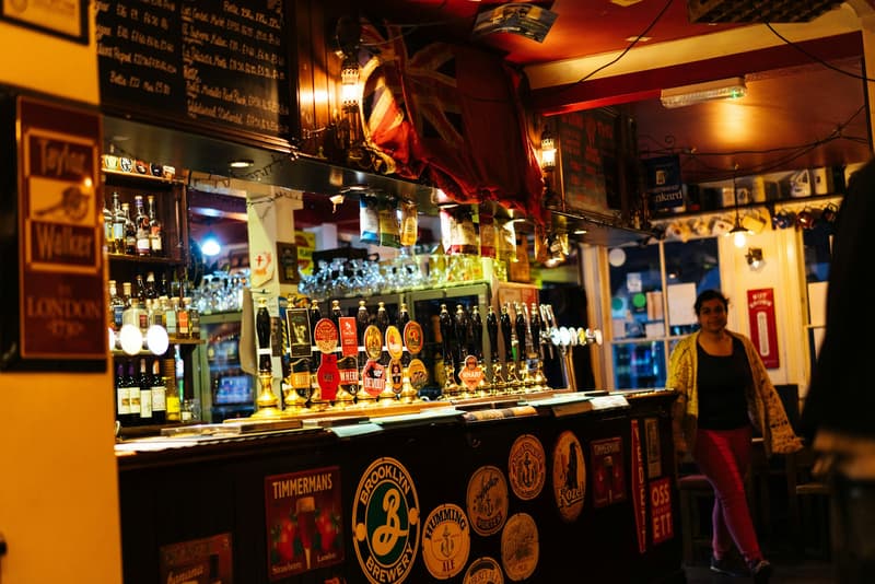 Barra concurrida de un pub londinense con grifos de cerveza, botellas y una bandera británica