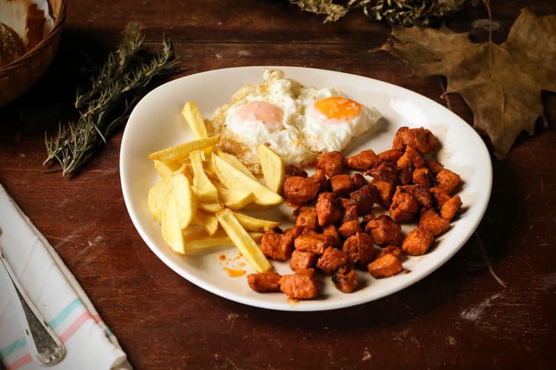 Assiette d'œufs au plat avec des pommes de terre taillées à la main et des dés de viande épicée sur bois sombre