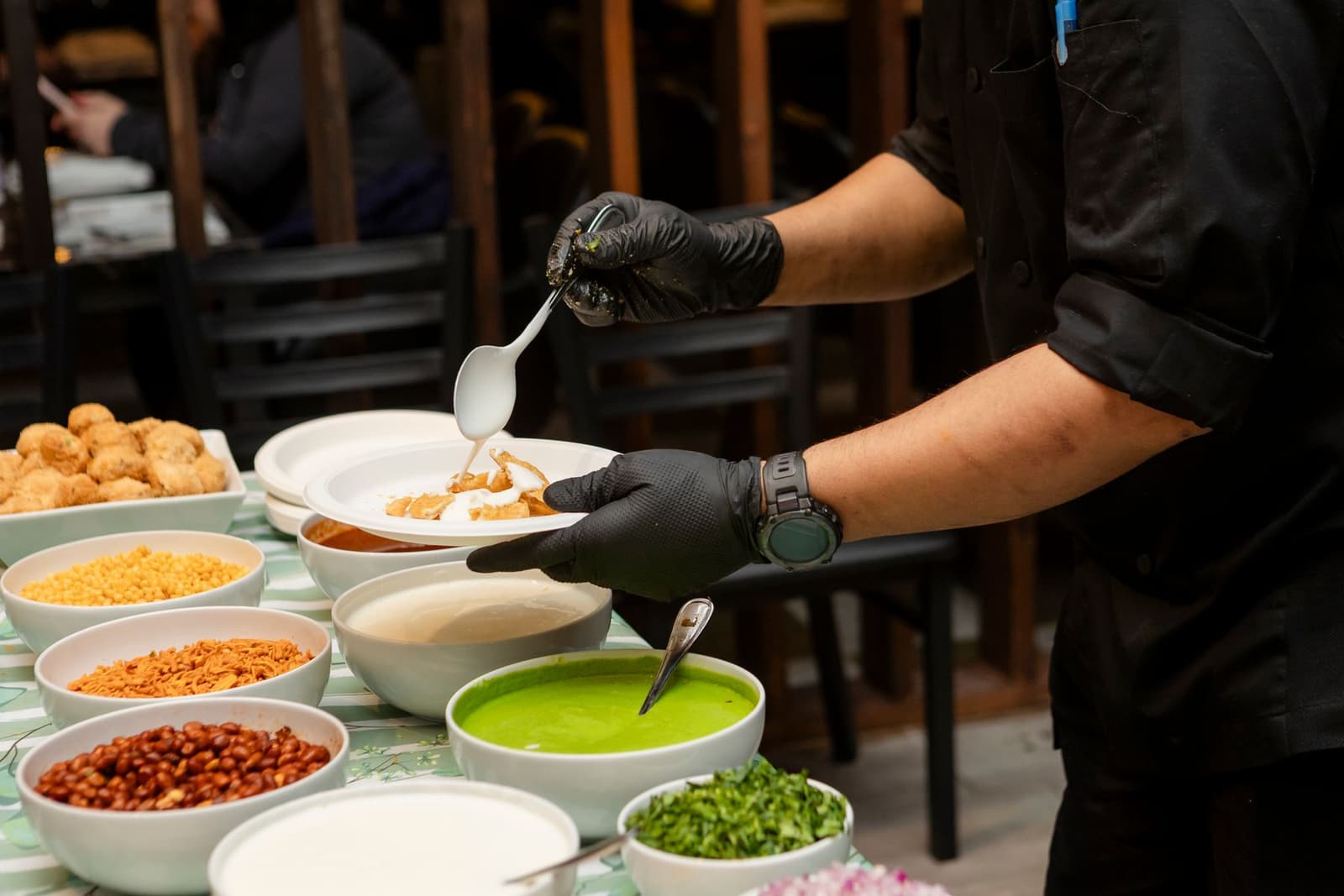 Chef che prepara un piatto di chaat accanto a ciotole di chutney e guarnizioni