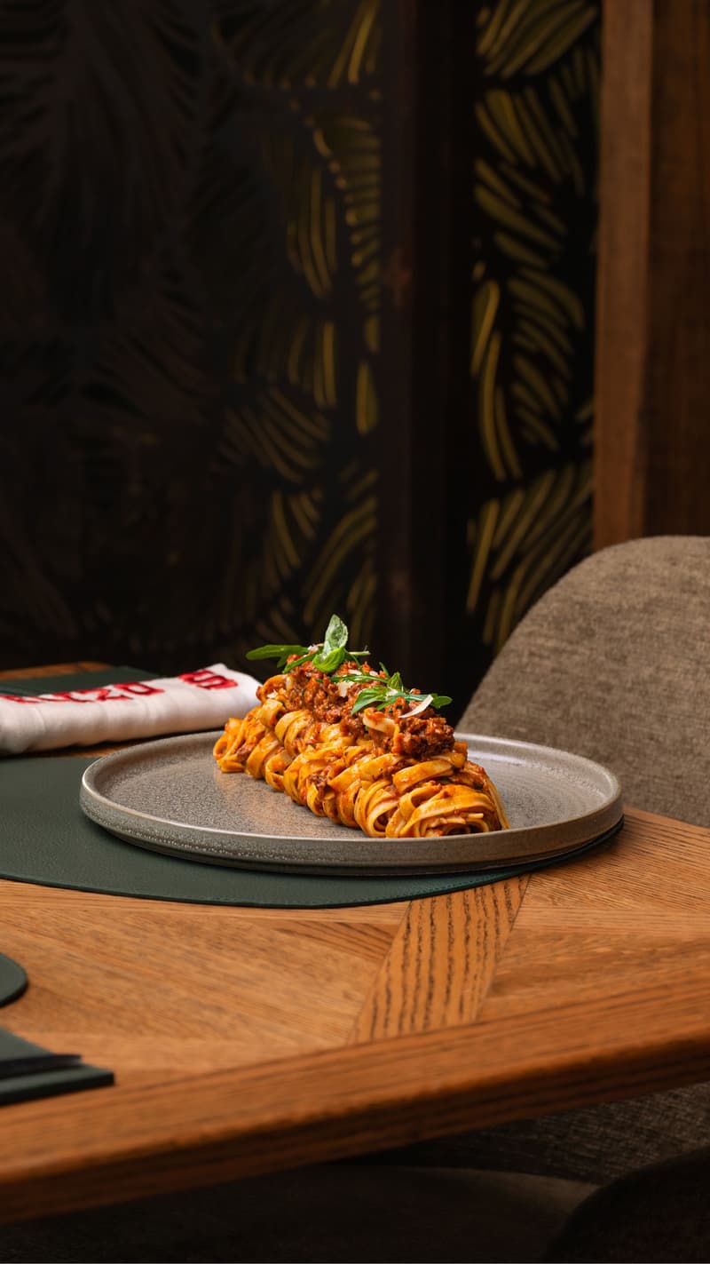 Un plat de tagliatelles dressé avec sauce et herbes sur une table de restaurant élégant