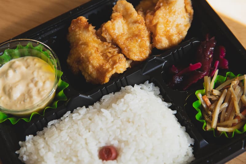 Bento à emporter dans une barquette en plastique noir avec poulet frit, riz et pickles