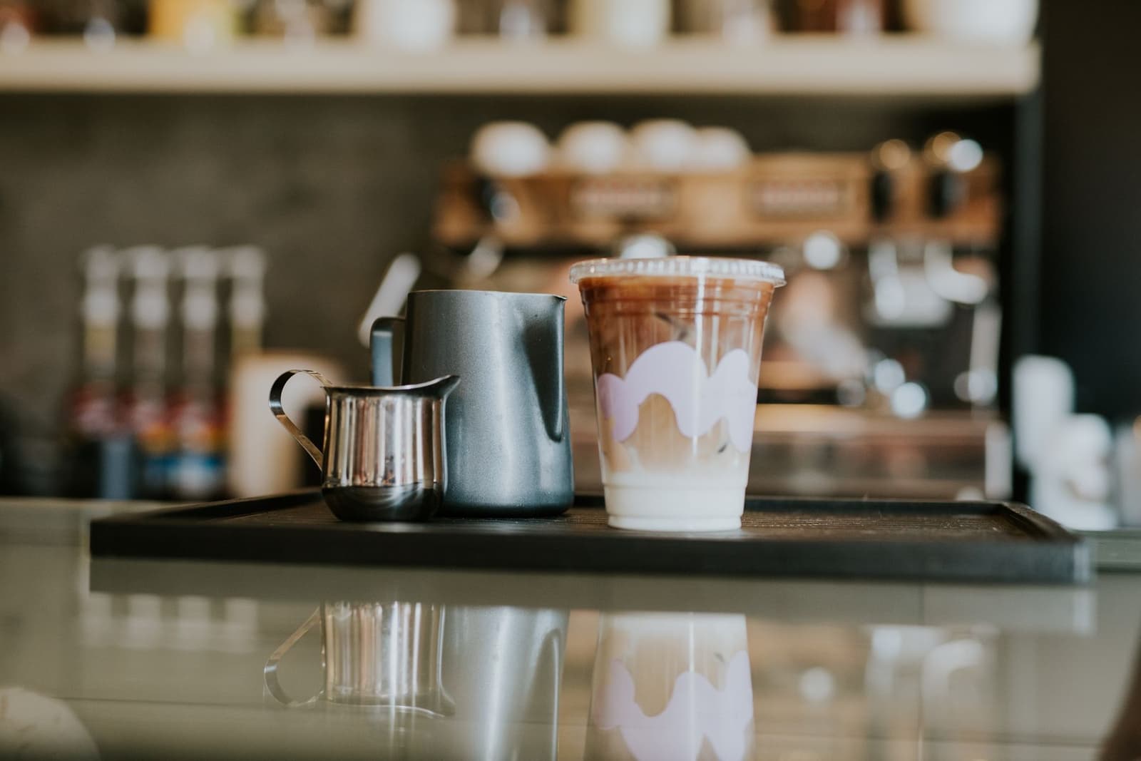 Iced coffee cup and metal creamers on a coffee shop counter tray