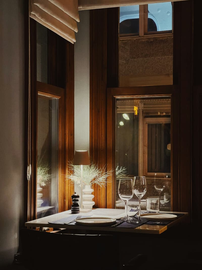 Un elegante tavolo da ristorante apparecchiato con calici accanto a una finestra alta