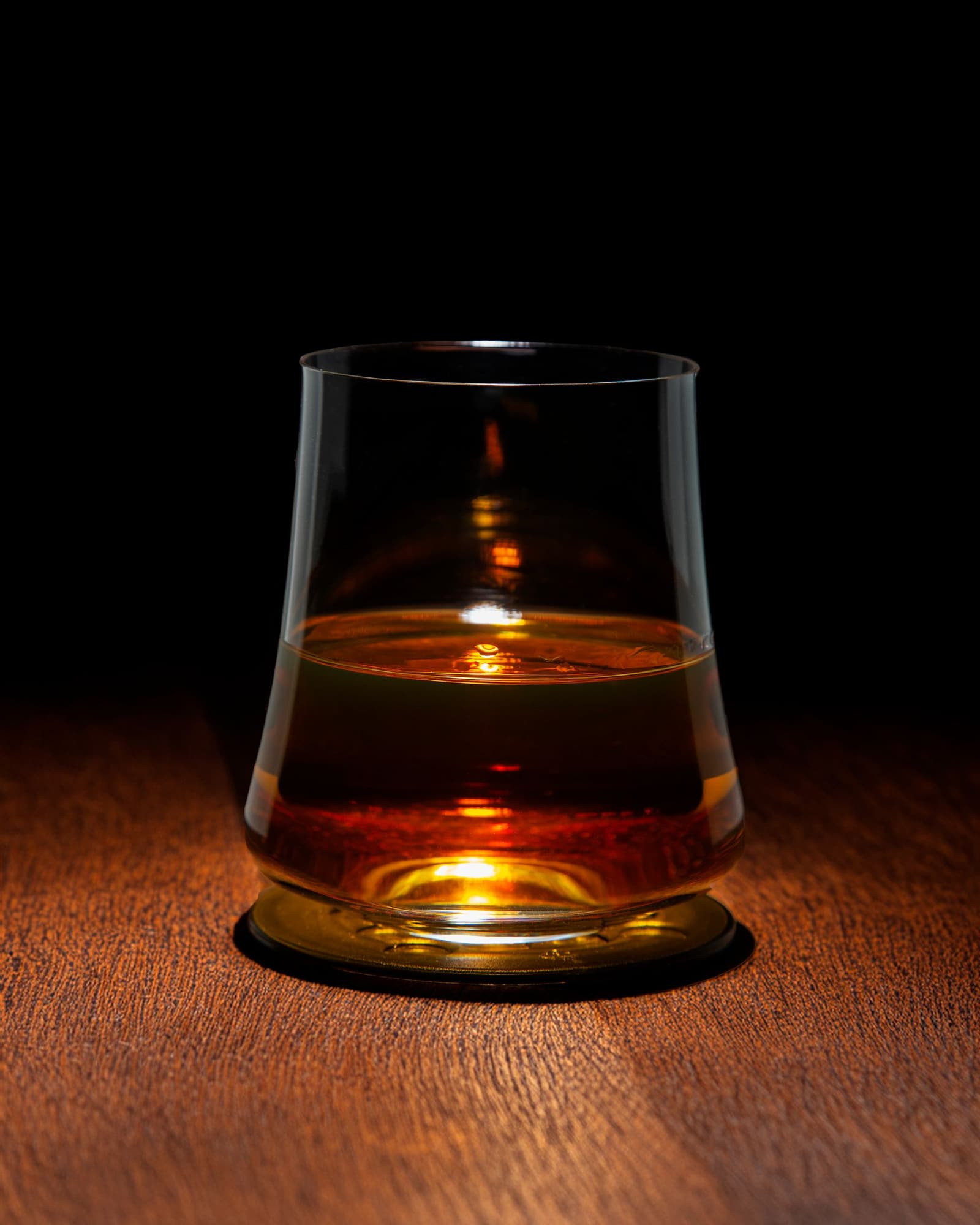Glass of amber whisky lit from below on a dark wooden table