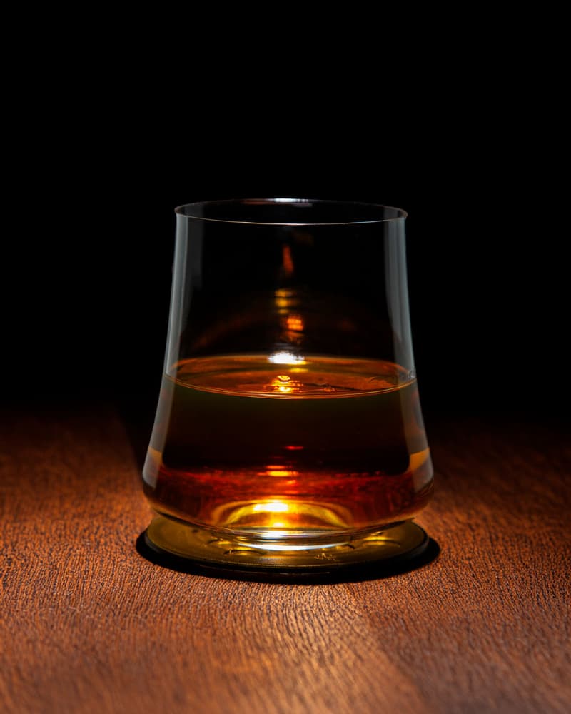 Glass of amber whisky lit from below on a dark wooden table