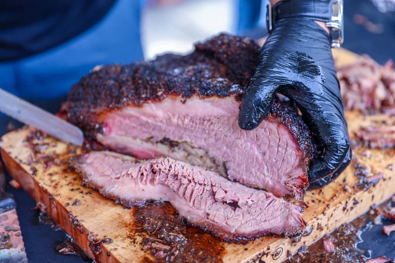 Mains gantées tranchant un brisket fumé sur une planche en bois