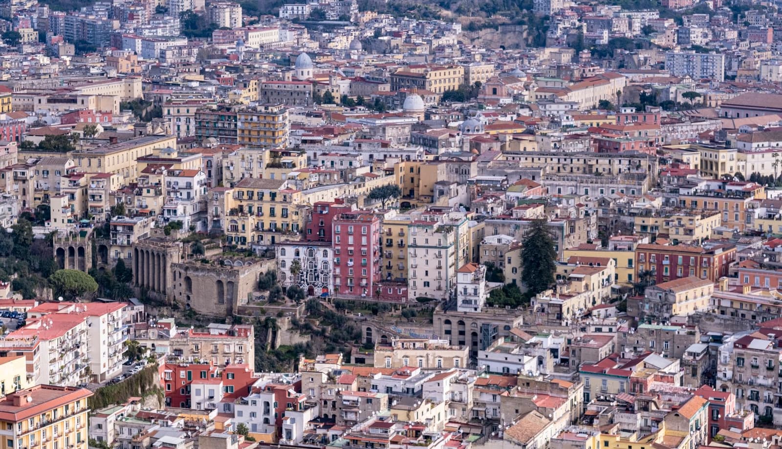 Vue aérienne de Naples avec des bâtiments aux couleurs pastel et des ruines antiques sur une colline
