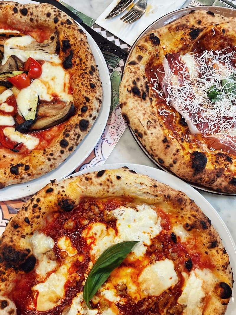 Trois pizzas napolitaines à la croûte boursouflée et légèrement brûlée sur une table en marbre