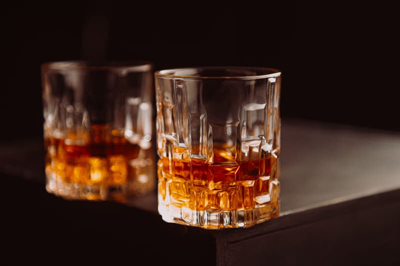 Two crystal glasses of Japanese whisky catching warm light on a dark wooden bar