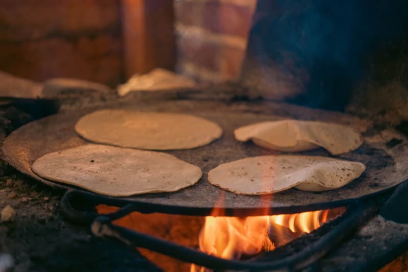 Tortillas di mais appena cotte su un comal a legna su fuoco vivo