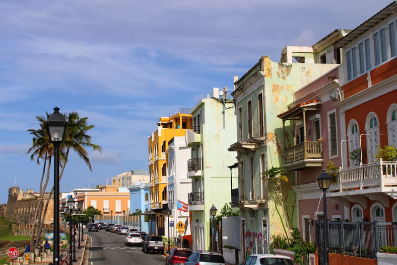 Bunte Kolonialhäuser mit Balkonen und Palmen in einer sonnigen Straße der Altstadt von San Juan