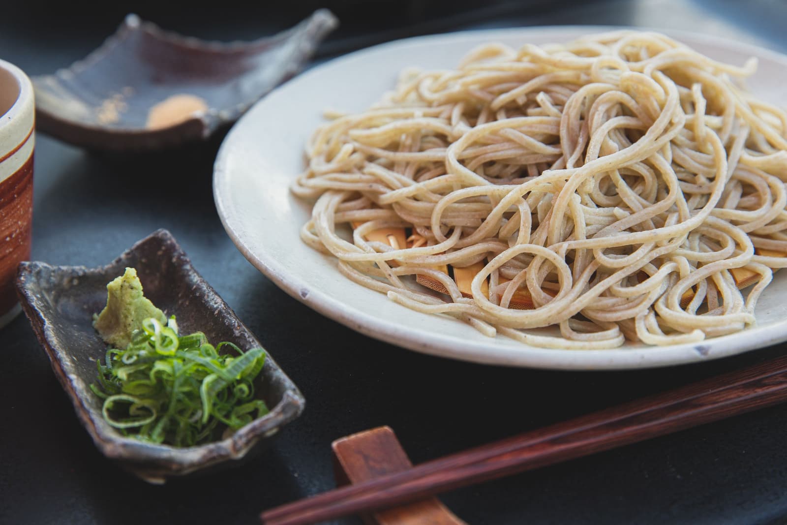 Teller mit Buchweizen-Soba, Wasabi, Frühlingszwiebeln und Essstäbchen auf dunklem Tisch