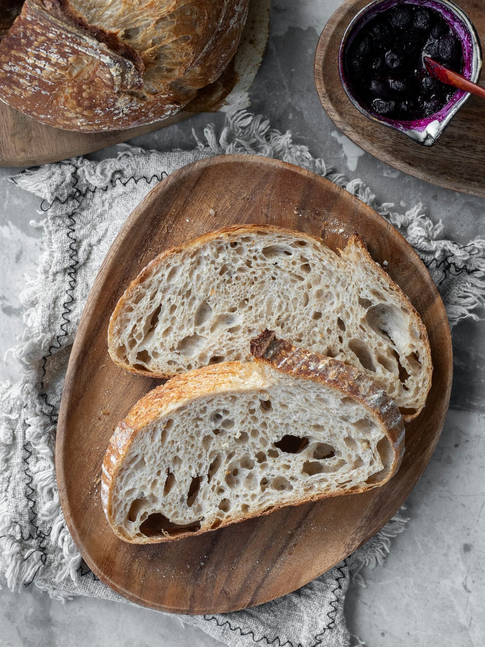 A round, floury sourdough loaf sliced open beside two slices on a wooden board