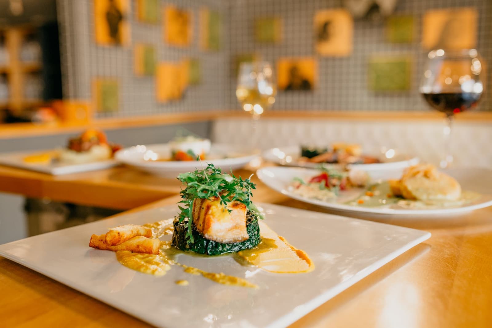 Plated fine-dining dishes and wine glasses on a restaurant counter