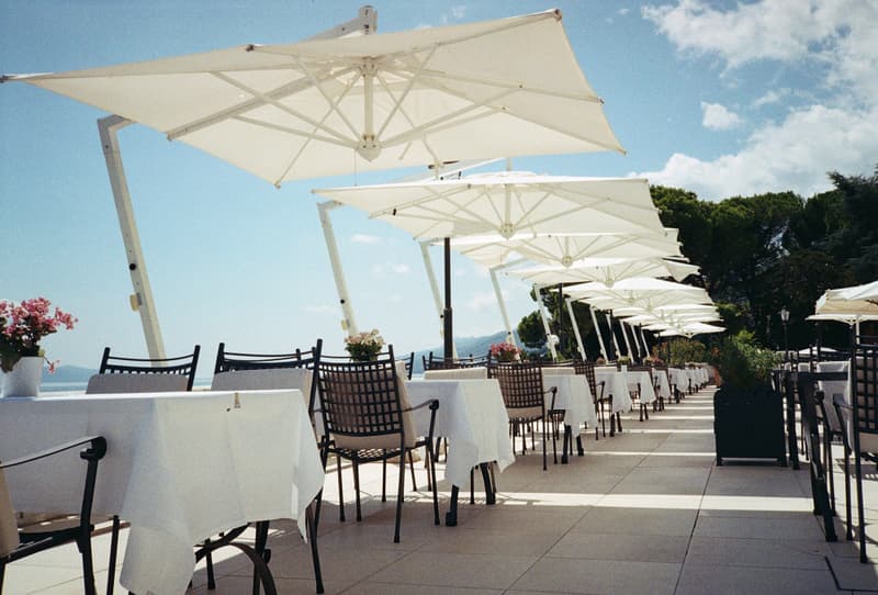 Sombrillas blancas sobre mesas con manteles en una terraza de restaurante mediterráneo