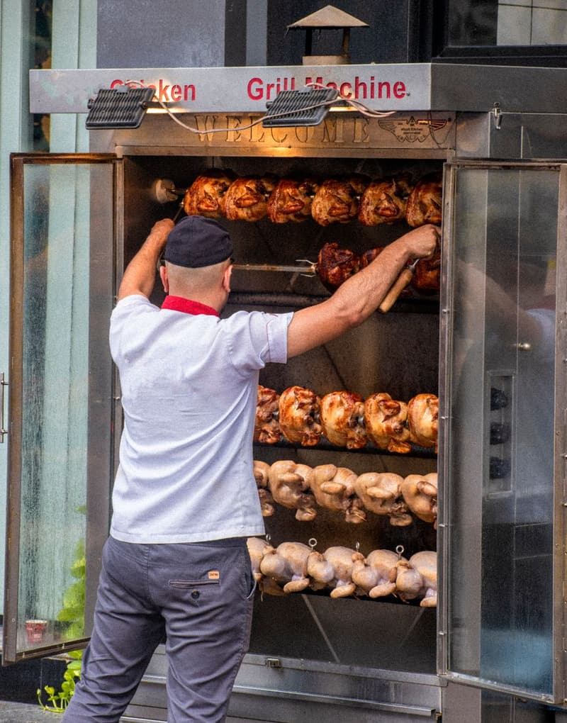 A chef loads whole chickens onto a rotisserie skewer inside a wood-fired grill