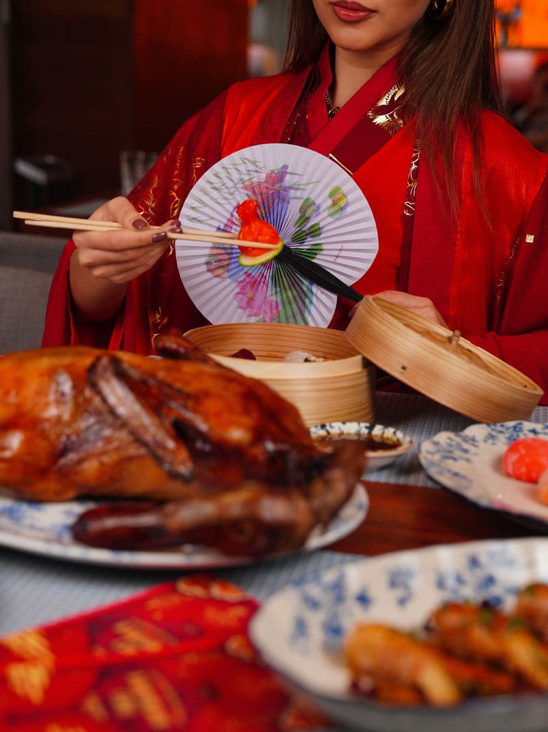 Pato pekinés entero servido en una mesa con cestas de dim sum y guarniciones