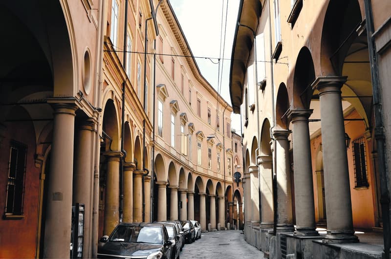 Sunlit porticoes lining a historic Bologna street with terracotta stone columns