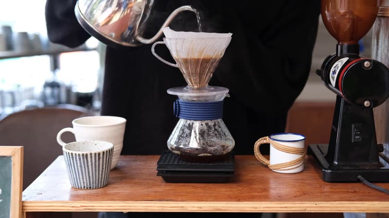 Des mains versant de l'eau chaude sur du café moulu dans un filtre pour-over