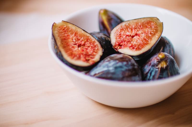Fichi viola maturi, uno tagliato a metà, in una ciotola bianca