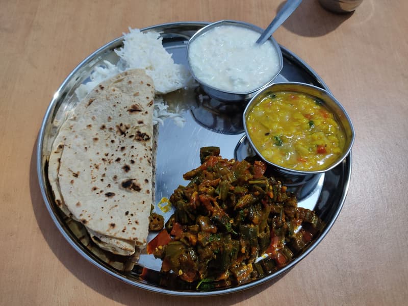 Piatto thali in acciaio con roti, riso, dal e okra su un tavolo di legno