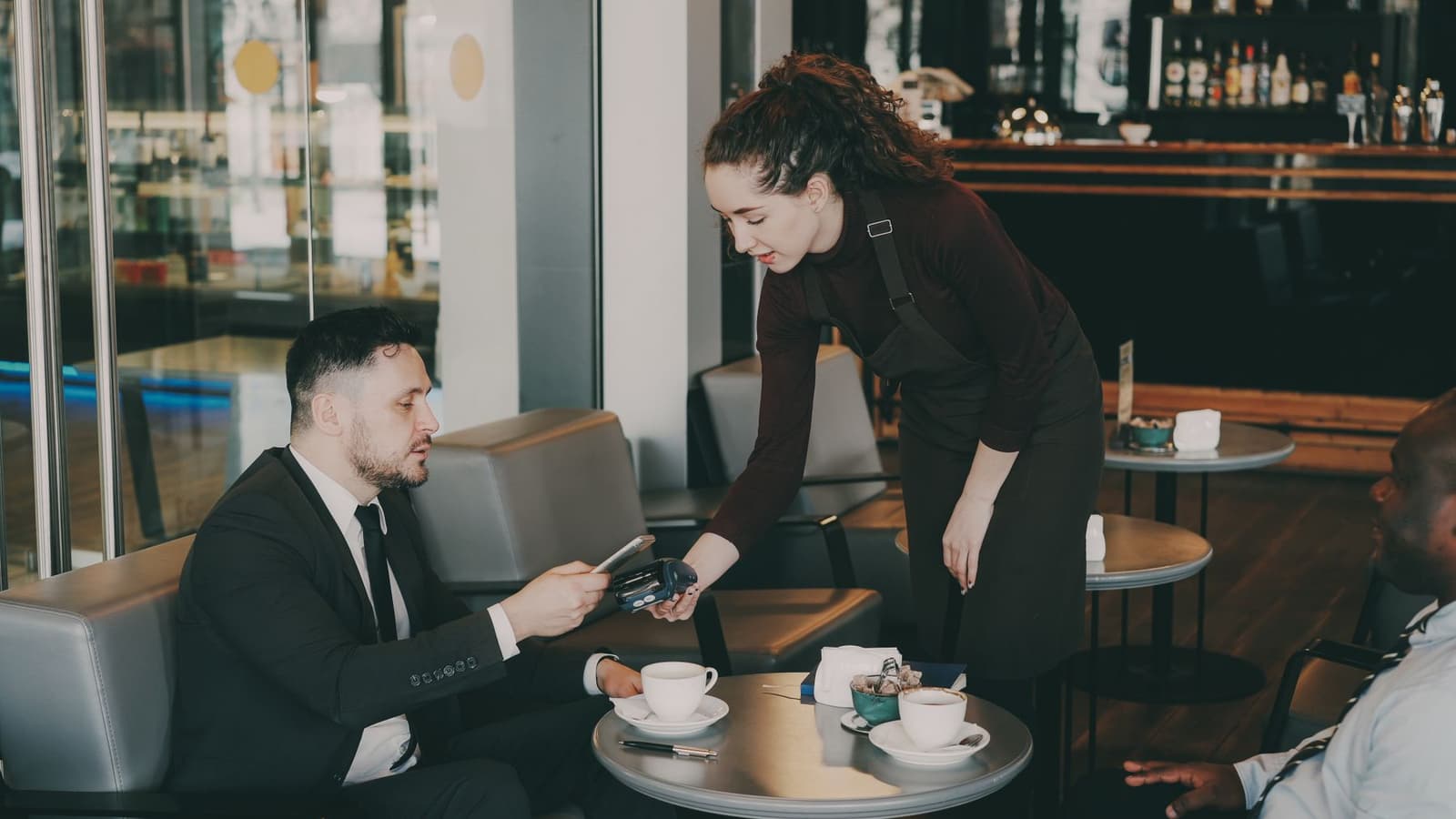 Serveuse tendant un terminal de paiement à un client attablé au café