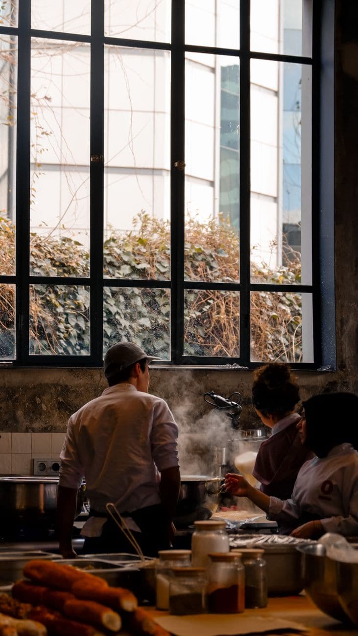 De jeunes chefs travaillant côte à côte au-dessus de poêles fumantes dans une cuisine ouverte de restaurant