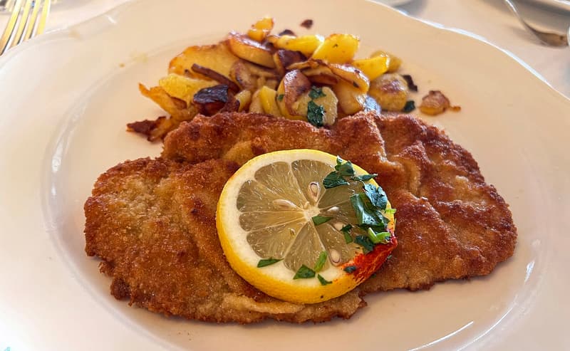 Cotoletta impanata con una fetta di limone e patate saltate su un piatto bianco