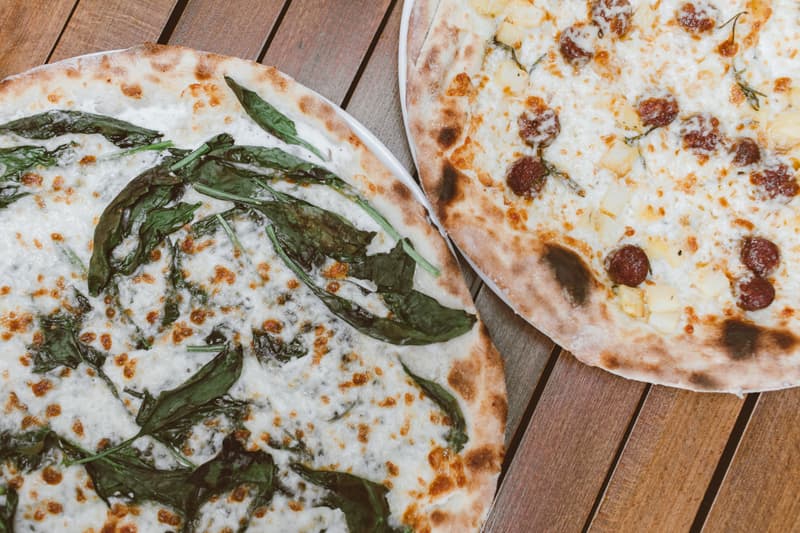 Dos pizzas redondas con espinacas y pepperoni sobre una mesa de madera
