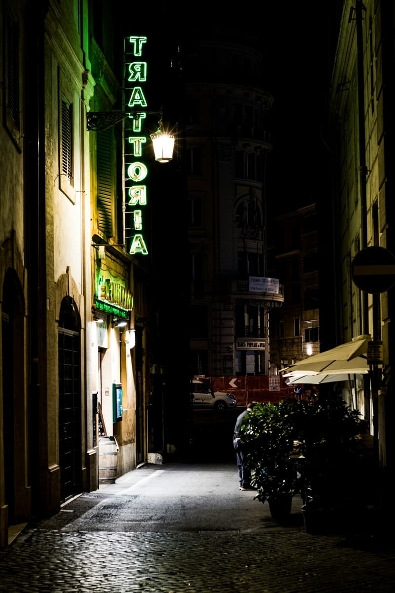 Un letrero de trattoria iluminado sobre un callejón de Roma de noche