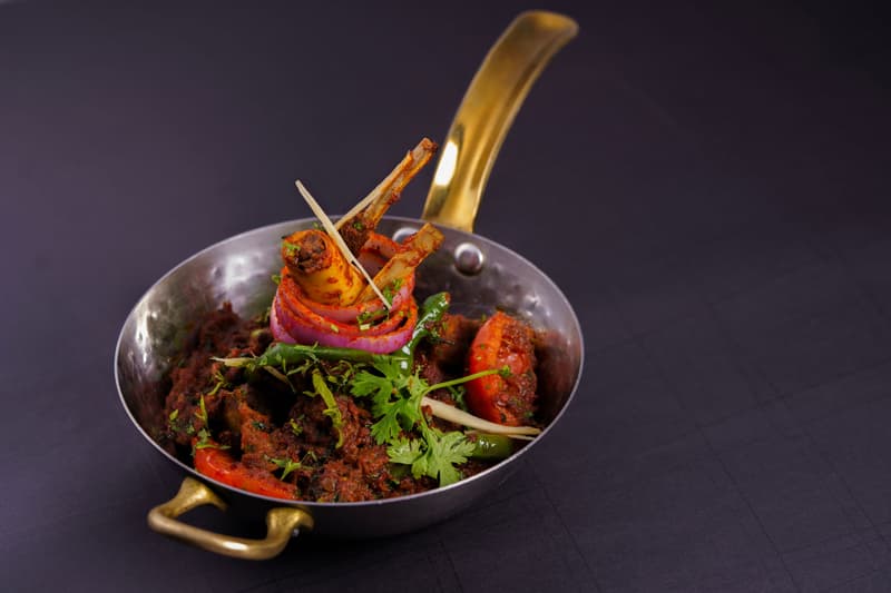 Costolette di agnello speziate e verdure servite in un kadai di metallo su un tavolo scuro