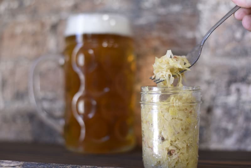 Chucrut casero en un tarro de cristal, levantado con un tenedor, junto a una cerveza