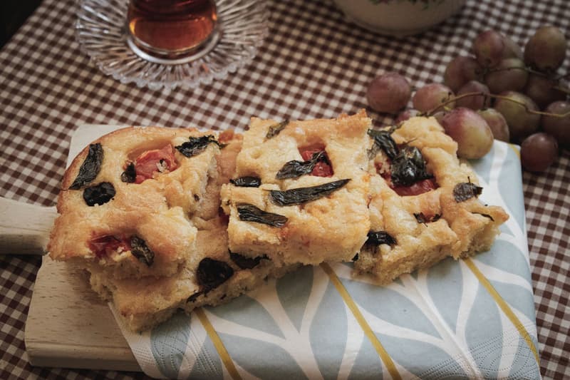 Schiacciata all'uva dorada recién horneada, cubierta de uvas negras enteras sobre una tabla de madera