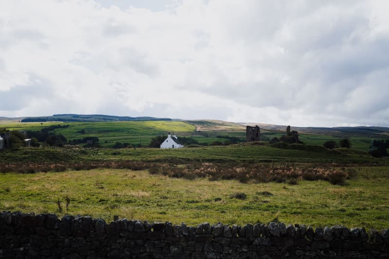 Scottish countryside with a ruined tower and a white cottage under a cloudy sky