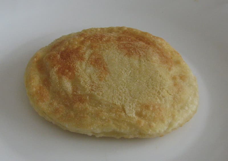 A golden fried seada on a white plate, waiting for its honey