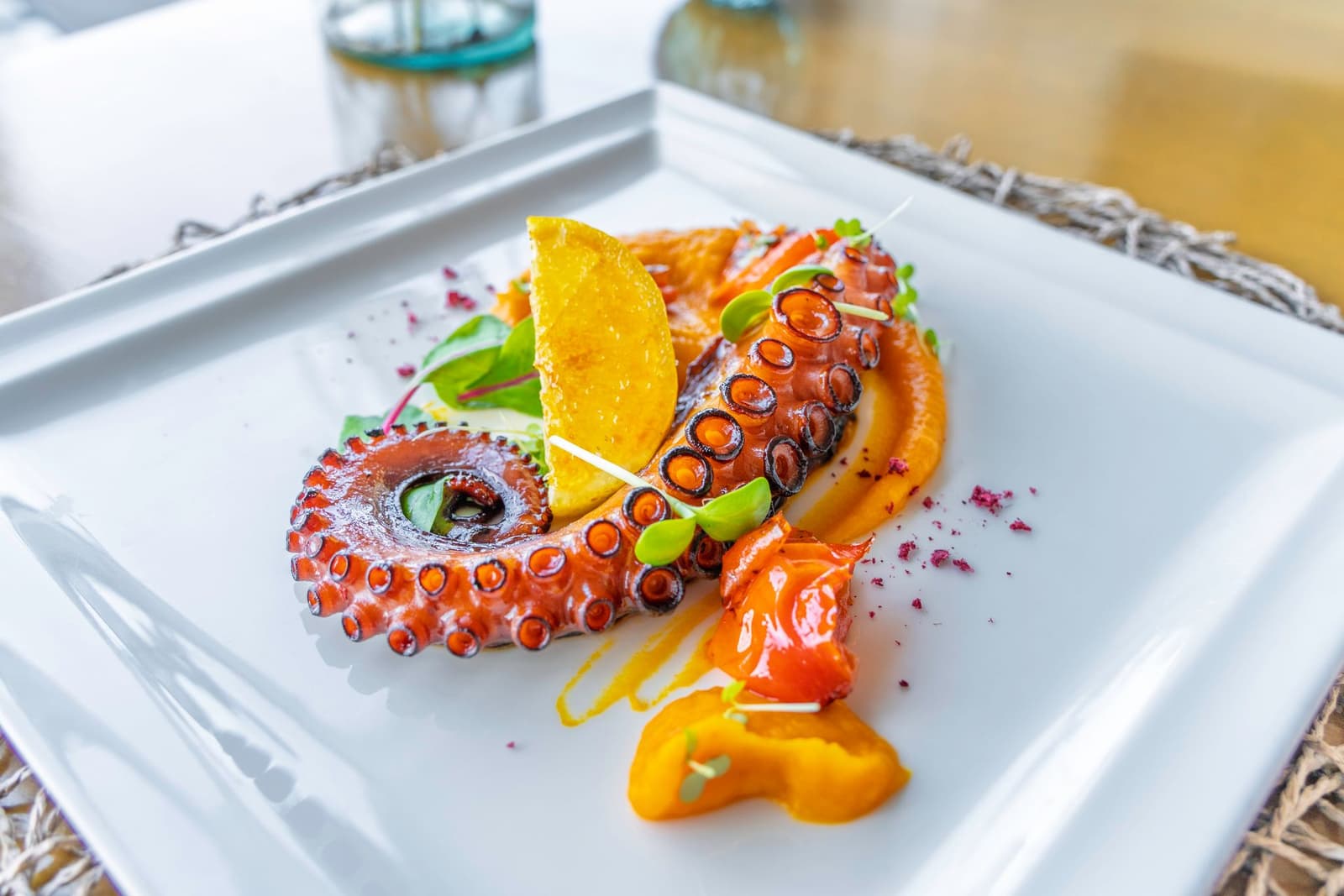 Tentáculo de pulpo a la brasa con puré de calabaza y cítricos en plato blanco