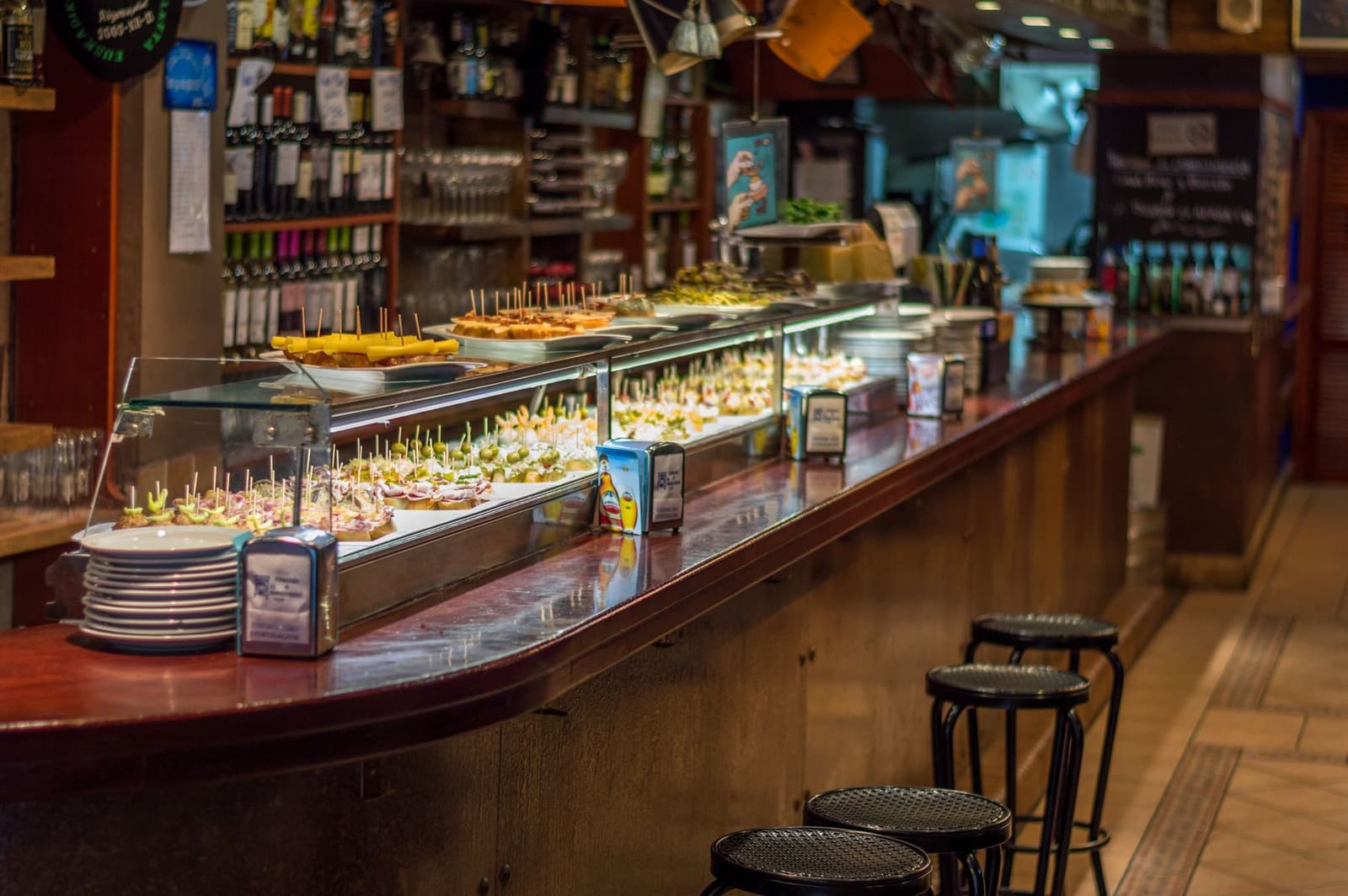 Een tapasbar-toog met pintxos en koude hapjes onder glas naast wijnflessen