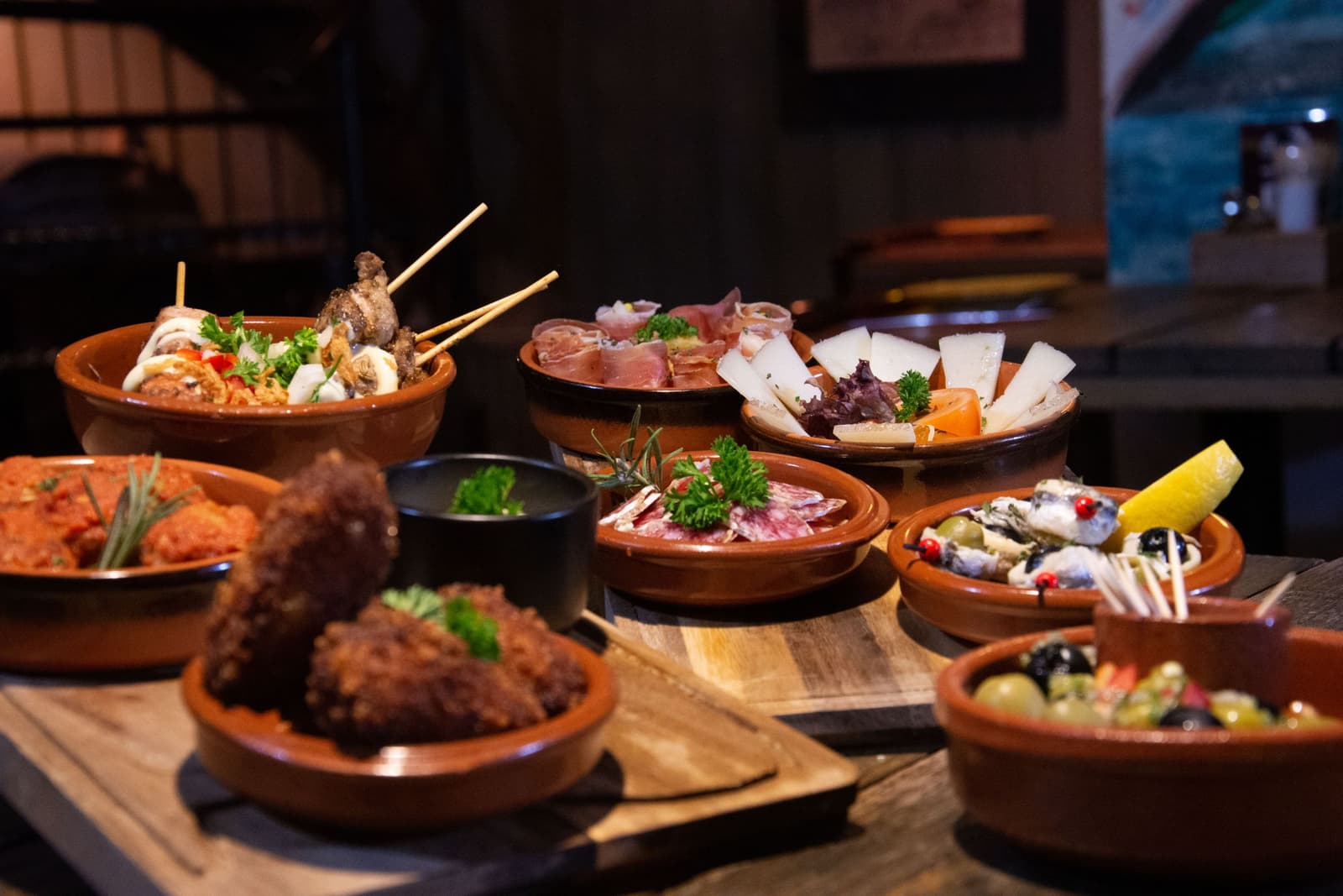 Tapas spagnole in cazuele di terracotta su taglieri di legno in un ristorante in penombra