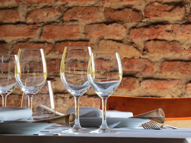 Copas de vino vacías y servilletas dobladas sobre una mesa de restaurante montada junto a una pared de ladrillo