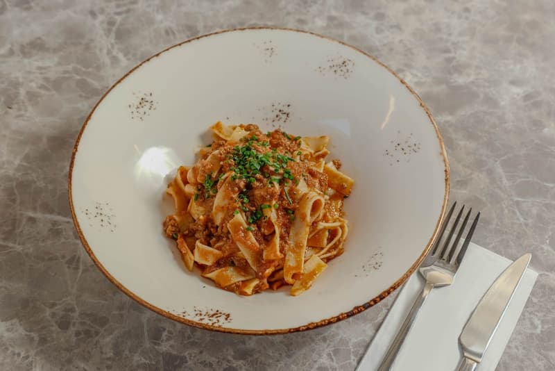 Tagliatelles fraîches aux œufs avec ragù de viande et ciboulette dans un bol blanc