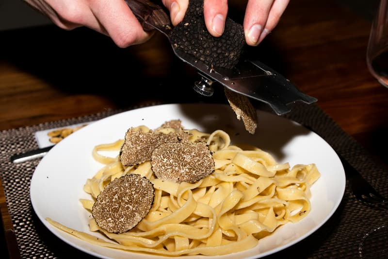 Une mandoline à truffe râpant de la truffe blanche fraîche sur un plat de pâtes en rubans