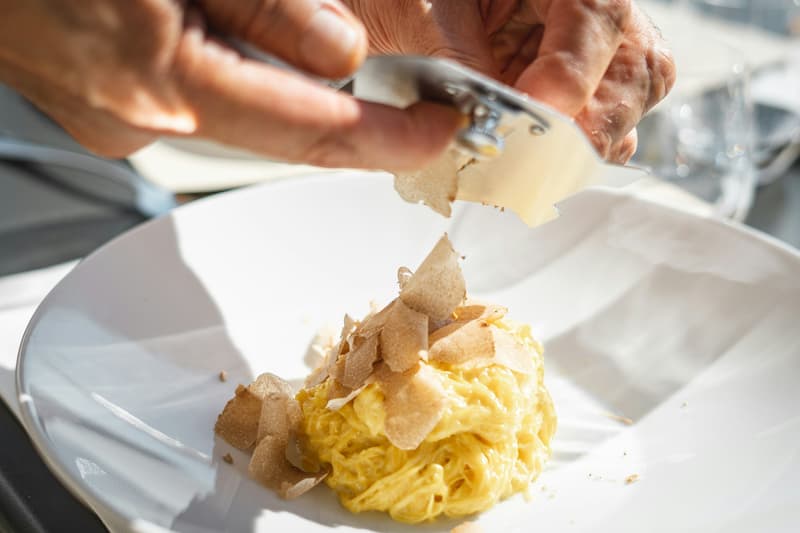 Trufa blanca rallada sobre un nido de tajarin al huevo en un plato blanco