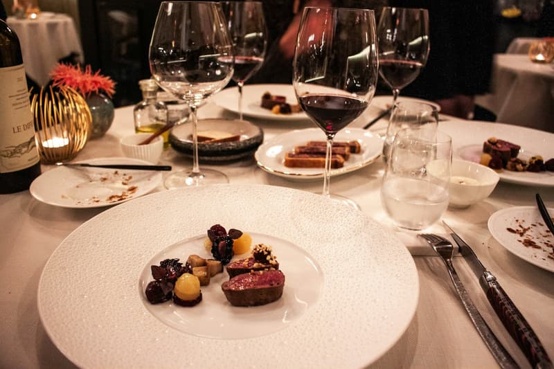 Une assiette de menu dégustation avec des verres de vin rouge sur une table de restaurant nappee de blanc