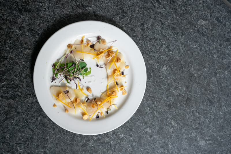 Piatto raffinato del menu degustazione con agrumi e germogli su marmo scuro