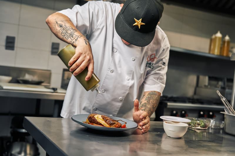 Chef en veste blanche et casquette noire qui dresse une assiette dans une cuisine professionnelle