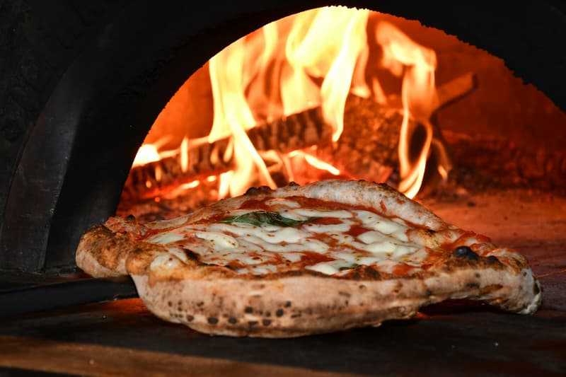 Margherita pizza with melted mozzarella baking inside a glowing wood-fired oven