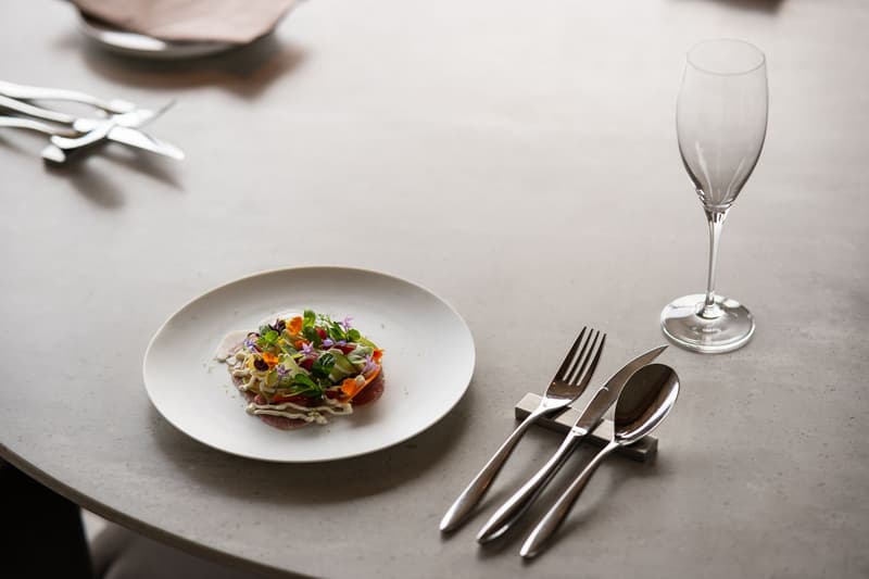 Single plated course, cutlery and an empty flute on a pale stone table