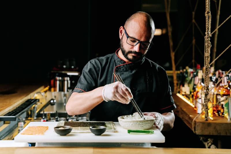 Chef plating nigiri sushi with chopsticks at a counter