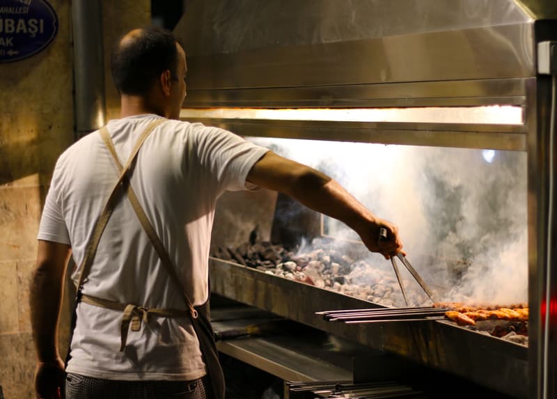 Un cuoco gira spiedini di carne sulla brace ardente di una griglia a carbone aperta
